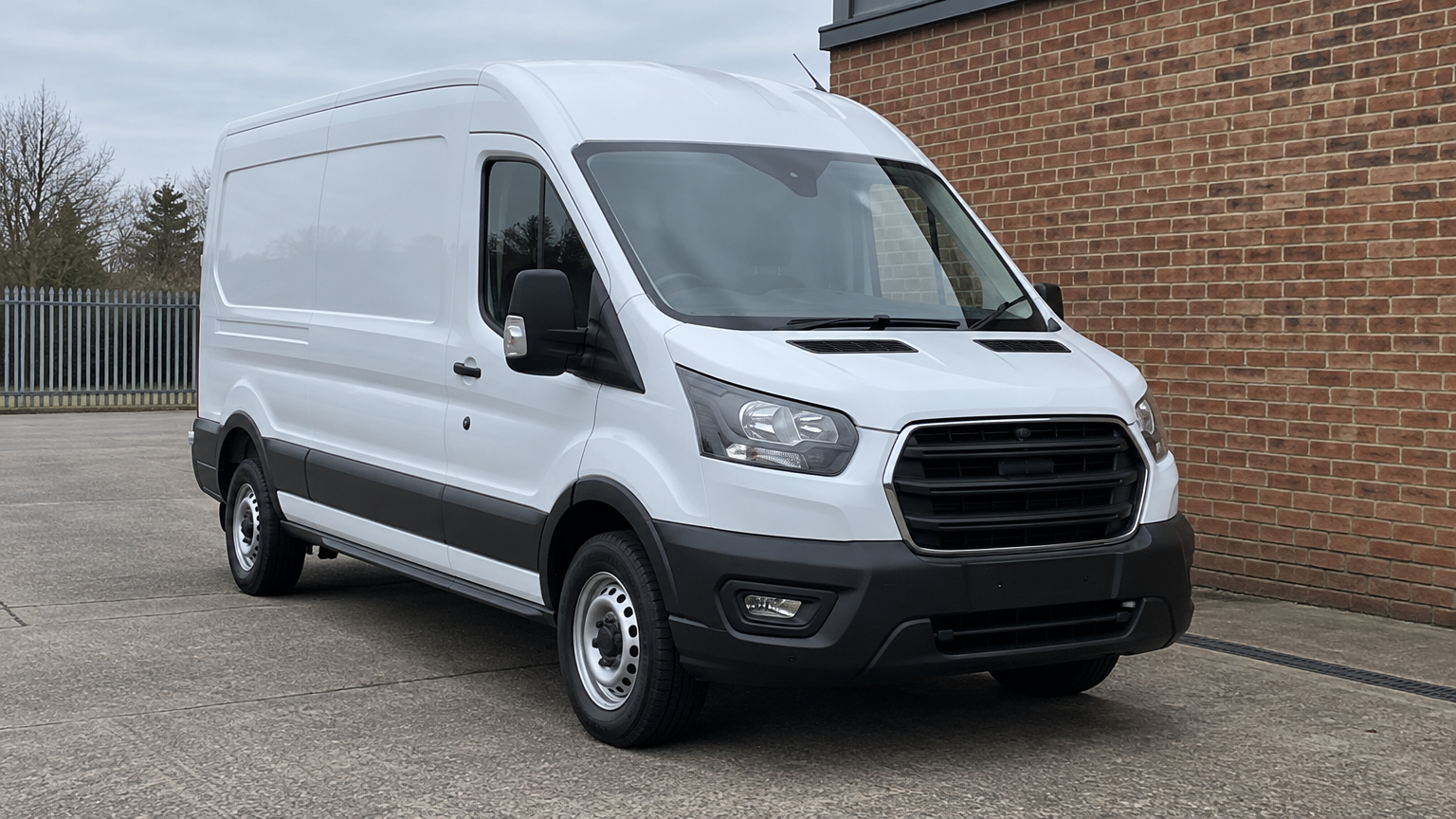Illustrative white Ford Transit panel van parked beside a brick building in a UK business yard.